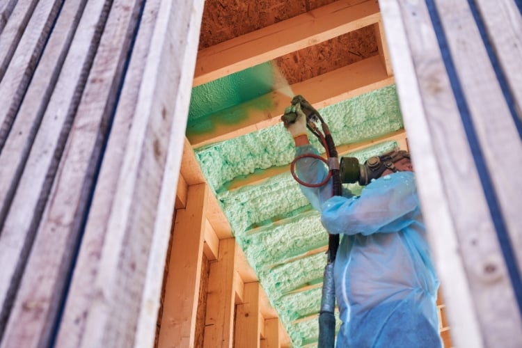 A worker is installing spray foam onto a ceiling